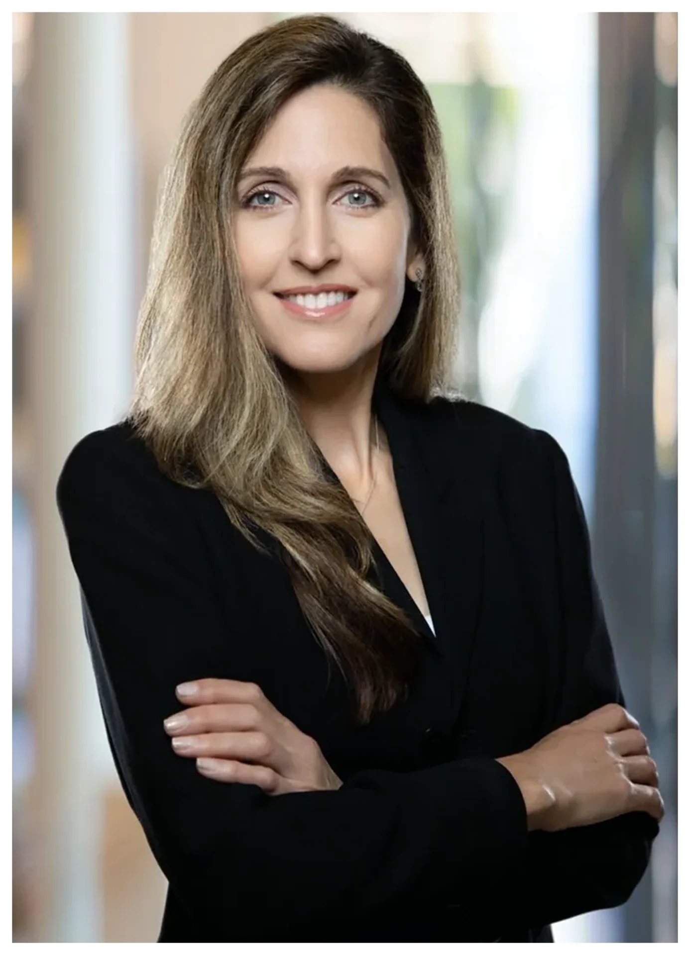 Smiling woman in black blazer, arms crossed.